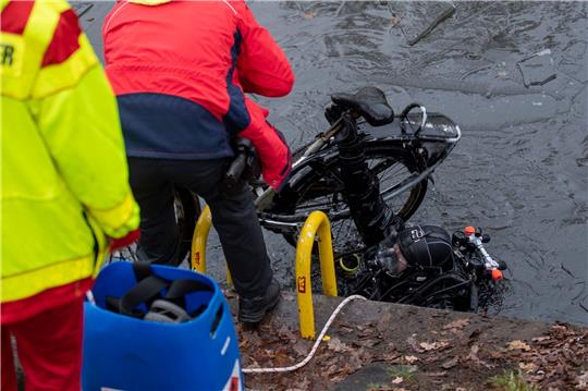 Ein Polizeitaucher hebt ein Fahrrad aus dem Schifffahrtskanal.