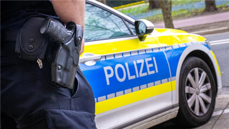Ein Polizist mit Waffe am Holster vor einem Polizeiauto.