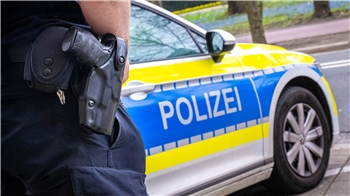Ein Polizist mit Waffe am Holster vor einem Polizeiauto.