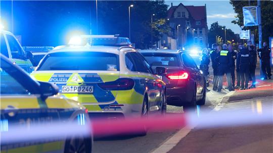 Polizisten und Polizeifahrzeuge stehen hinter einer Absperrung.