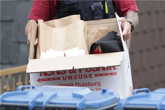 Ein Polizist trägt nach einer Wohnungsdurchsuchung einen Karton mit sichergestellte Gegenständen.