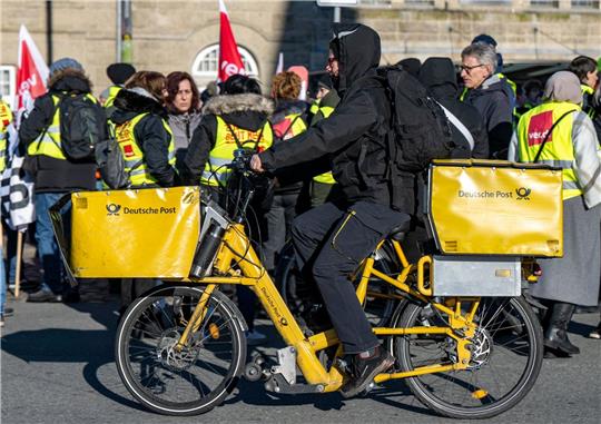 Ein Postbote radelt in Bielefeld an Streikenden einer Verdi-Aktion vorbei.