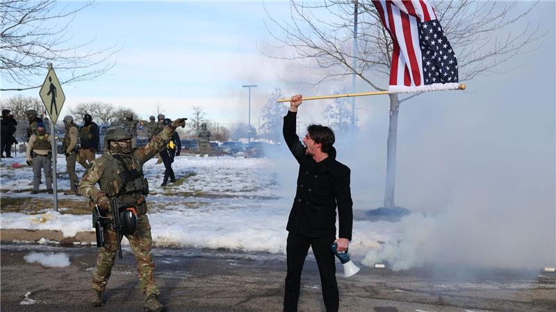 Proteste nach tödlichen Schüssen in Minneapolis halten an Ein Protestierender mit einer amerikanischen Flagge steht einem ICE-Beamten gegenüber.