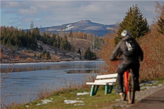 Ein Radfahrer ist an der teils zugefrorenen Talsperre mit Sicht auf den niedersächsischen Wurmberg unterwegs. Foto: Matthias Bein/dpa