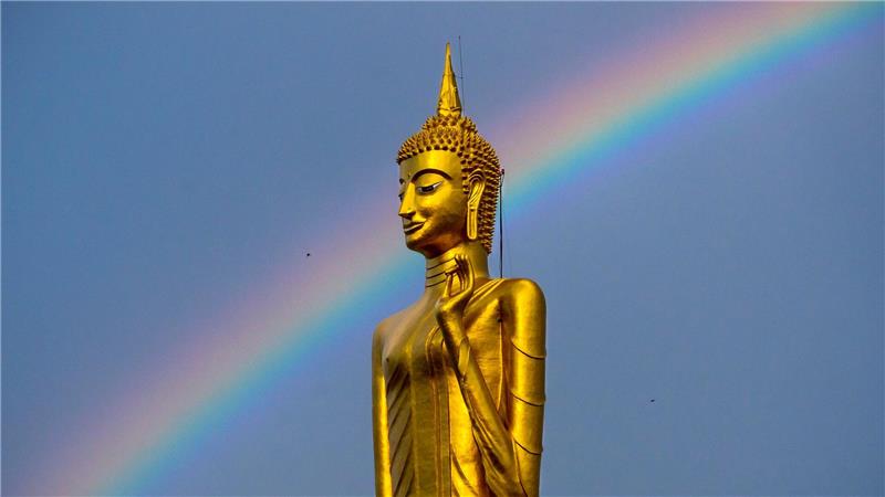 Ein Regenbogen ist hinter der stehenden Buddha-Statue Luang Pho Yai des Wat Buraphaphiram in Roi Et, Thailand, zu sehen.