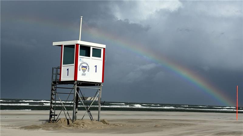 Ein Regenbogen steht an einem Himmel voll dunkler Wolken über der Nordsee und über der Insel Juist. 