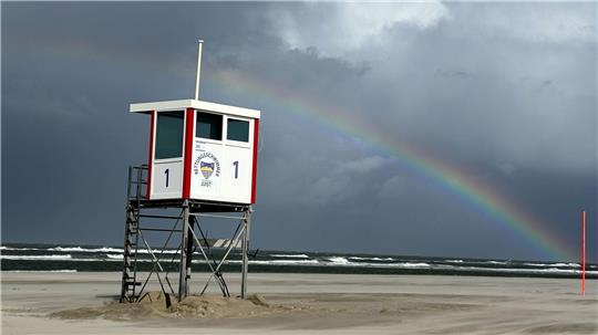 Ein Regenbogen steht an einem Himmel voll dunkler Wolken über der Nordsee und über der Insel Juist. 