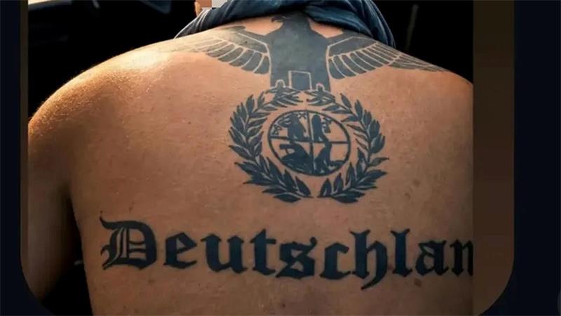 Rückenansicht eines Mannes mit großem schwarzen Tattoo eines Adlers über einem Lorbeerkranz mit einem Wappen in der Mitte.