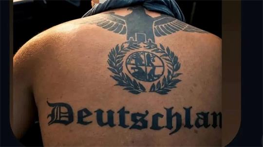 Rückenansicht eines Mannes mit großem schwarzen Tattoo eines Adlers über einem Lorbeerkranz mit einem Wappen in der Mitte.