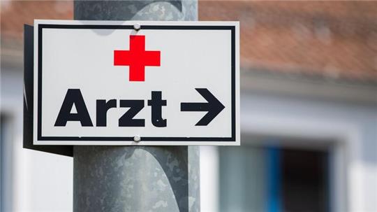 Ein Schild mit der Aufschrift „Arzt“ hängt an einer Straßenlaterne.