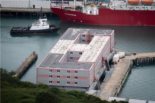 Ein Schleppschiff passiert im Hafen von Portland in Dorset das Schiff «Bibby Stockholm», das bis zu 500 Menschen aufnehmen soll.