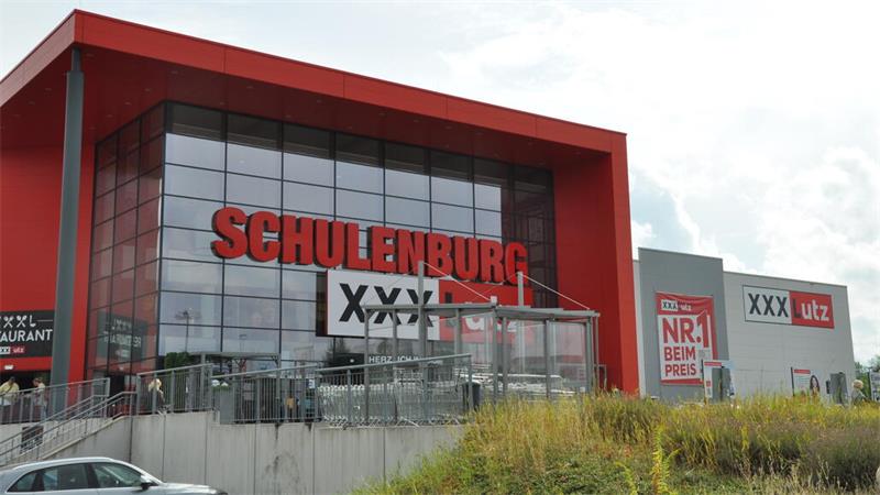 Großes modernes Gebäude mit rotem Schriftzug 'SCHULTENBURG' und Werbetafeln mit 'XXXL' und 'utz'
