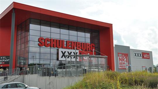 Großes modernes Gebäude mit rotem Schriftzug 'SCHULTENBURG' und Werbetafeln mit 'XXXL' und 'utz'