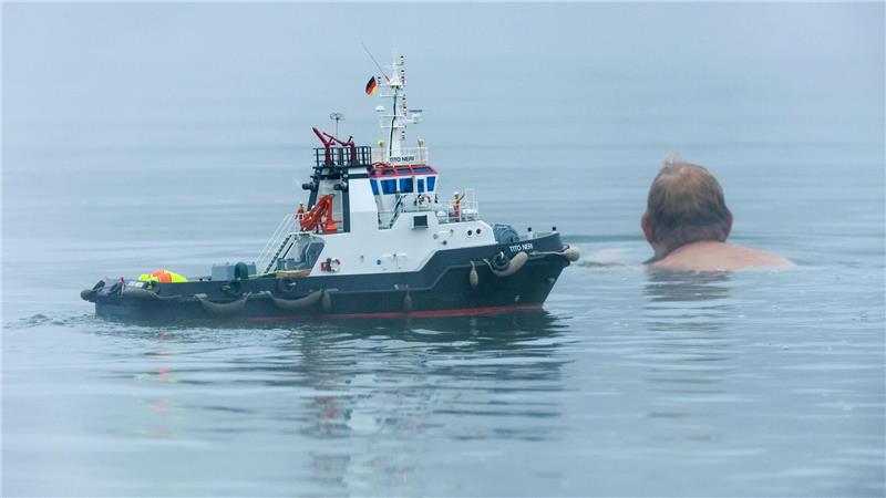 Ein Schwimmer und ein Modellboot in Form eines Schleppers sind im Nebel im Schwarzachtalsee unterwegs.