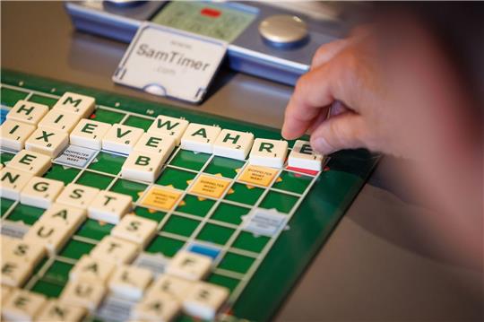 Ein Scrabble-Spieler sitzt an einem Spieltisch anlässlich der 14. Deutschen Scrabble-Meisterschaft in Minden und legt ein Wort in deutscher Sprache.
