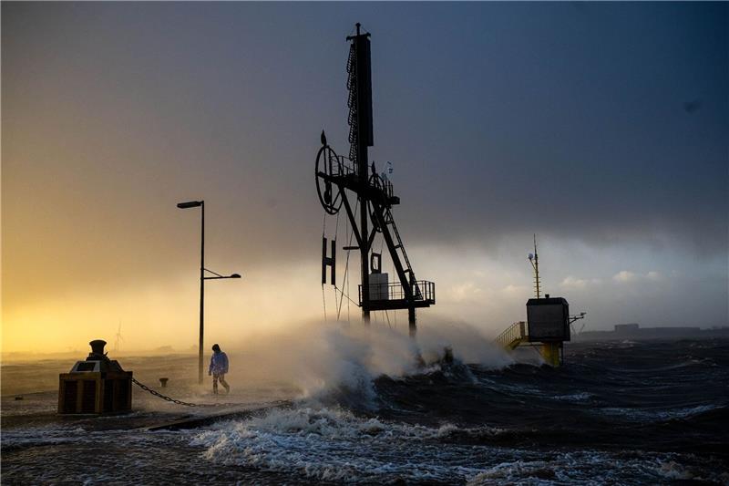 Nach Sturmtief: Heftige Regenfälle und Schnee erwartet Ein Spaziergänger läuft bei Sturmflut und Wellen am Ufer der Wesermündung in Bremerhaven entlang.
