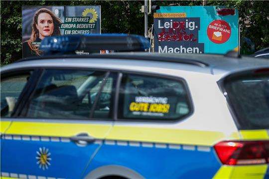Ein Streifenwagen der Polizei fährt an Wahlplakaten vorbei.