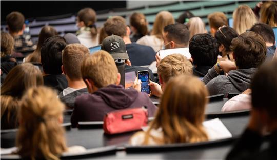 Ein Student spielt am Smartphone während einer Vorlesung.