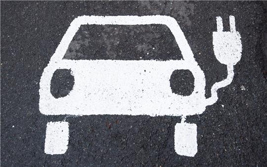 Ein Symbol für ein Elektroauto markiert einen Parkplatz neben einer E-Ladesäule.