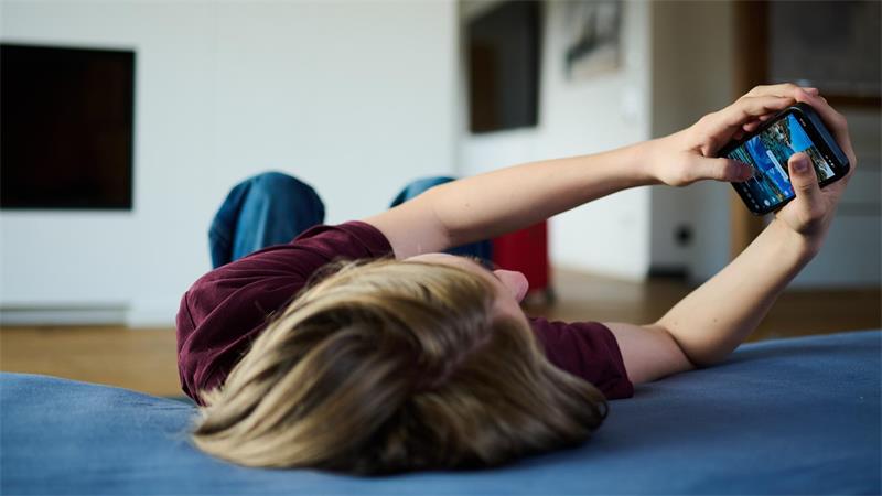 Ein Teenager liegt auf einer Matratze und schaut auf sein Handy.