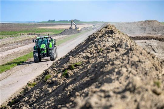Ein Traktor fährt an einer Baustelle an einem Deich vorbei.