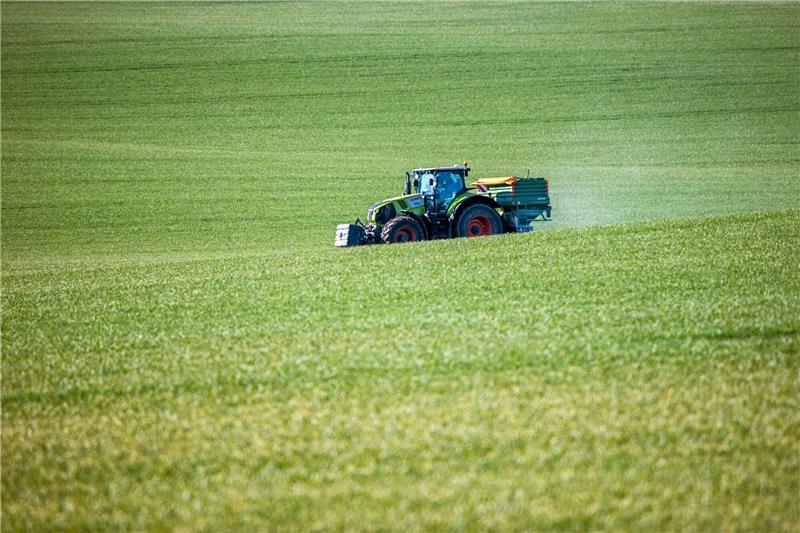 Ein Traktor mit einem Streuaufsatz verteilt Dünger auf einem Feld.