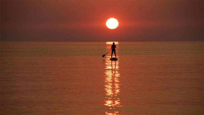 Ein Urlauber steuert bei Sonnenuntergang vor der Küste von Jantarny dem früheren ostpreußischen Palmnicken, einem Ferienort in der westrussischen Region Kaliningrad, ein Stand-up-Paddleboard.