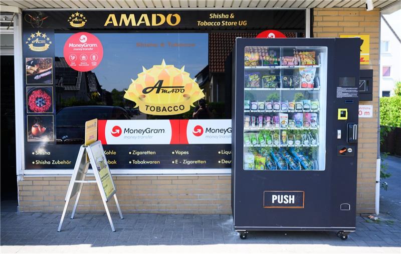 Ein Warenautomat, unter anderem mit Lachgasflaschen bestückt, steht vor einem Ladengeschäft.