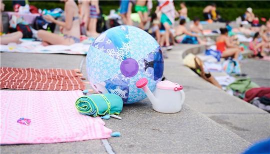 Ein Wasserball und Handtücher liegen in einem Schwimmbad am Beckenrand.