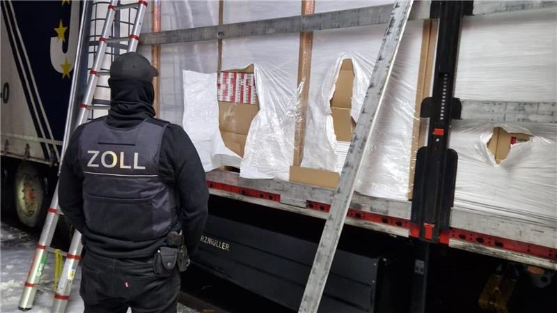 Ein Zöllner steht vor einem mit Zigaretten beladenem Lkw.