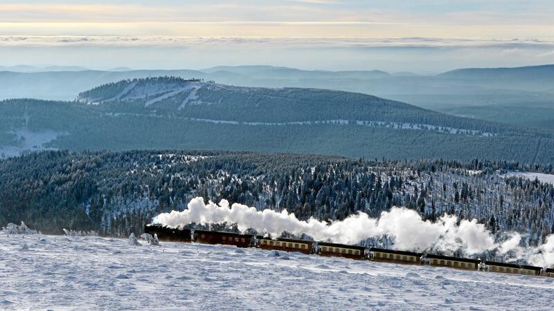 Ein Dampflok fährt mit mehreren Anhängern durch den Schnee.