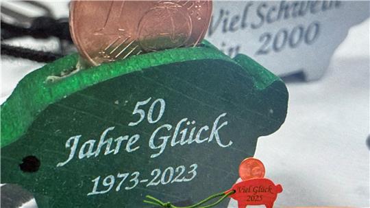 Ein aktuelles Glücksschweinchen steht vor einem Foto seiner älteren Geschwister. Am morgigen Dienstag werden die Talismane wieder in Braunlage und St. Andreasberg von den Kommunalpolitikern zum Kauf angeboten, die sich in den Dienst der guten Sache stellen.