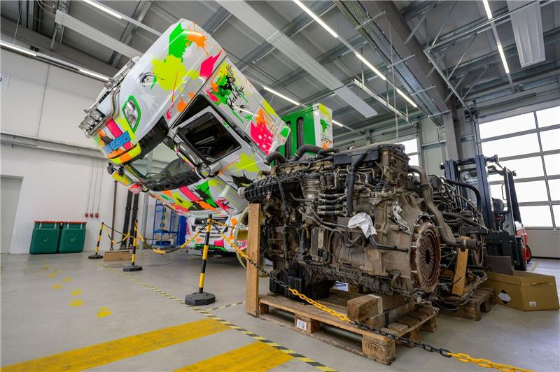 Ein ausgebauter Dieselmotor lagert vor einer LKW Zugmaschine die mit Wasserstoff betrieben wird, steht in einer Werkhalle der Clean Logistics.