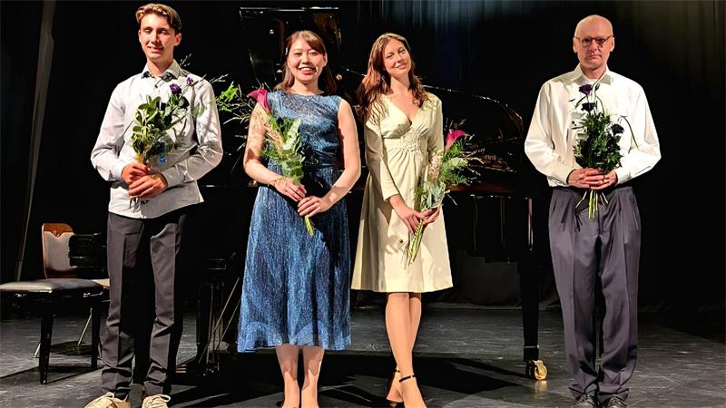 Zwei Männer und zwei Frauen stehen vor einem Piano mit jeweils einer Blume in der Hand.