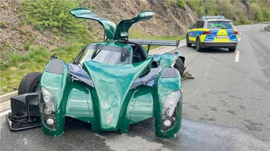 Ein grüner Wagen mit offenen Flügeltüren steht auf einer Landstraße. Dahinter ist ein Polizeiauto zusehen.