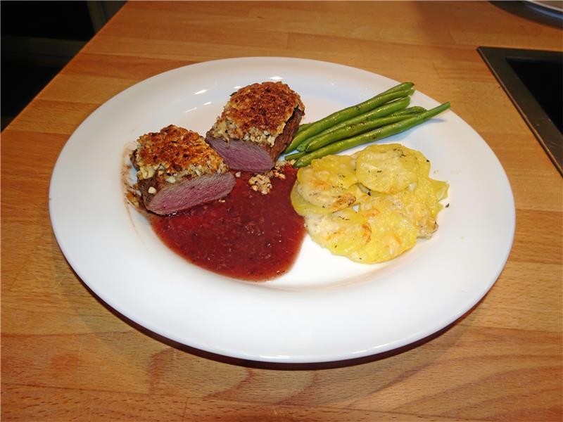 Frisch aus dem Wald und Bio pur Ein genussvoller Klassiker: Saftiger Rehrücken unter der Haselnusskruste mit Sauerkirschsauce, in Butter geschwenkten Prinzessbohnen und einem kleinen Kartoffelgratin. Foto: Horn