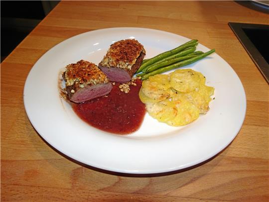 Ein genussvoller Klassiker: Saftiger Rehrücken unter der Haselnusskruste mit Sauerkirschsauce, in Butter geschwenkten Prinzessbohnen und einem kleinen Kartoffelgratin. Foto: Horn
