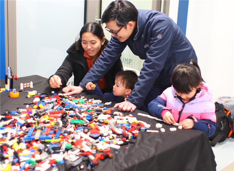 Eine asiatische Familie spielt an einem Tisch mit Legosteinen.