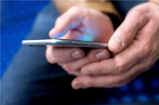 Ein junger Mann sitzt in einer S-Bahn und benutzt dabei sein Smartphone.