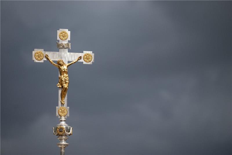 Christliche Geistliche fordern Ausbau der Suizidprävention Ein katholisches Kruzifix ist vor dunklen Wolken zu sehen.