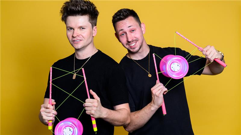 Zwei junge Männer in schwarzen T-Shirts präsentieren pinkfarbene Diabolos.