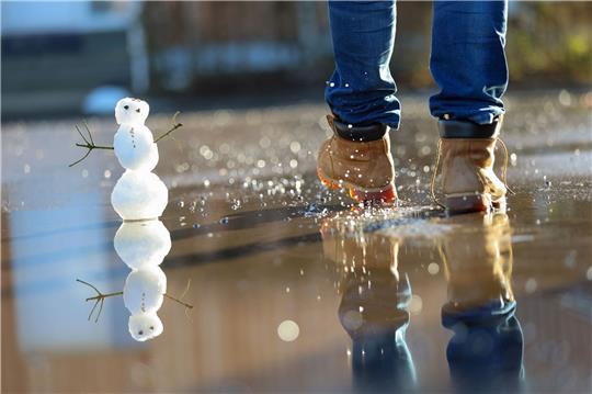 Ein kleiner Schneemann in einer Pfütze.
