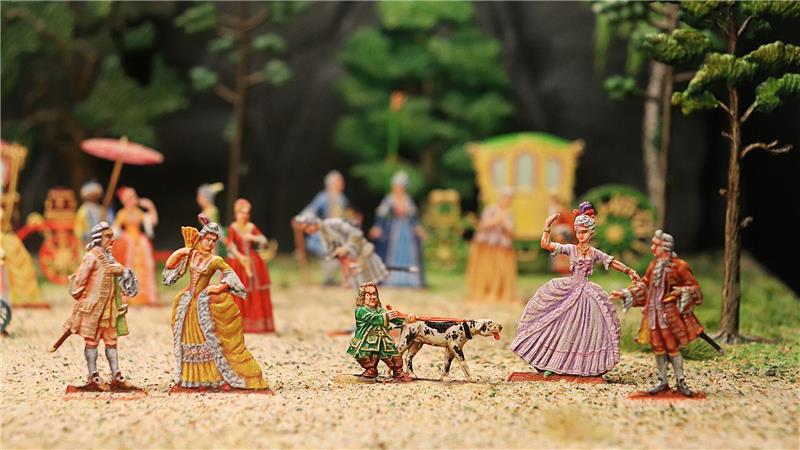 Perücken, Pomp und Pulverdampf im Goslarer Zinnfigurenmuseum Mehrere kleine, farbige Figuren in historischen Kostümen stehen auf einem sandigen Weg vor einem grünen Wald