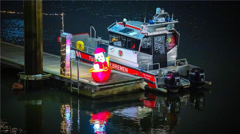 Ein leuchtender Weihnachtsmann steht neben einem Boot der Feuerwehr an der Weser in Bremen. 