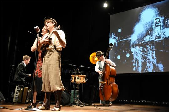 „Ein rätselhafter Schimmer“ lautet der Titel des Zwanziger-Jahre-Programms, vom Trio Größenwahn und dem Zeichner Robert Nippoldt virtuos und augenzwinkernd auf die Bühne des Kulturkraftwerks Harzenergie gebracht. Beim Couplet „Schöner Gigolo“ steuert Nippoldt (vorne) den Ukulelenpart bei. Foto: Kempfer