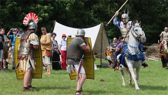 Ein Reiter stürmt mit einem Stoßwaffe auf Legionäre zu. 