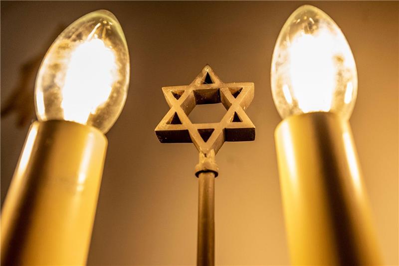 Ein siebenarmiger Leuchter (Menora) mit einem Davidstern in der Mitte leuchtet in einer Synagoge. Fragen zum Judentum werden auf einer Website beantwortet.