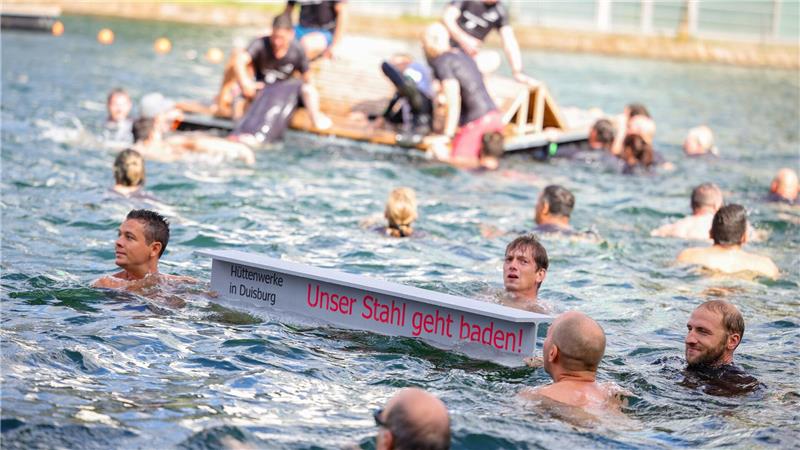 „Unser Stahl geht baden“: Stahlarbeiter springen ins Wasser Ein symbolischer Stahlträger mit dem Slogan der Demo schwimmt im Duisburger Innenhafen zwischen zahlreichen Stahlbeschäftigten.