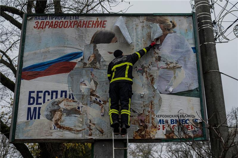 Krieg gegen die Ukraine: So ist die Lage Ein ukrainischer Feuerwehrmann reißt in der kürzlich befreiten Stadt Cherson eine russisches Werbeplakat von einer Werbetafel.