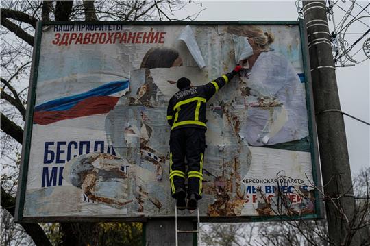 Ein ukrainischer Feuerwehrmann reißt in der kürzlich befreiten Stadt Cherson eine russisches Werbeplakat von einer Werbetafel.